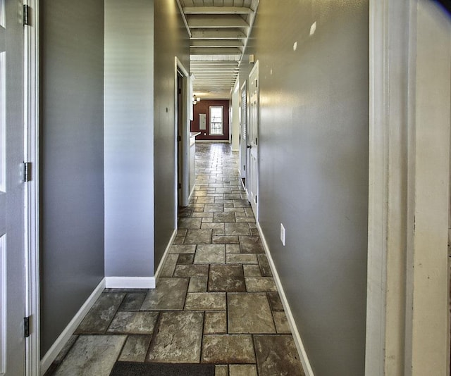 hall featuring stone tile flooring and baseboards