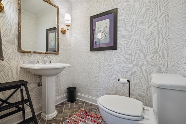 bathroom with wallpapered walls, brick floor, toilet, and baseboards