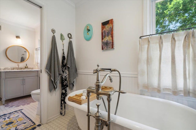 full bathroom featuring toilet, vanity, a freestanding bath, ornamental molding, and wainscoting