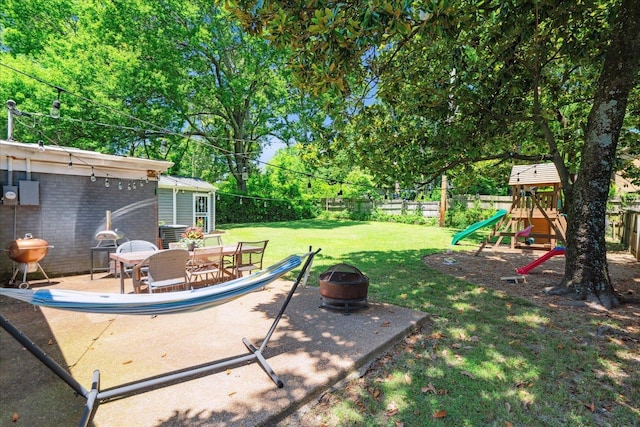 view of yard featuring a fire pit, a playground, a fenced backyard, and an outdoor structure