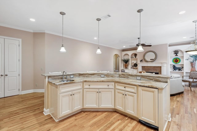 kitchen featuring ornamental molding, open floor plan, cream cabinetry, a fireplace, and a sink