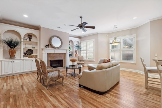 living area featuring a tile fireplace, baseboards, crown molding, and light wood finished floors