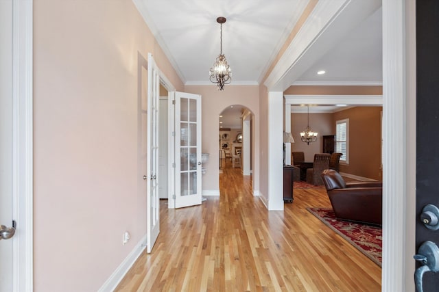 foyer entrance featuring arched walkways, light wood-style flooring, baseboards, ornamental molding, and an inviting chandelier