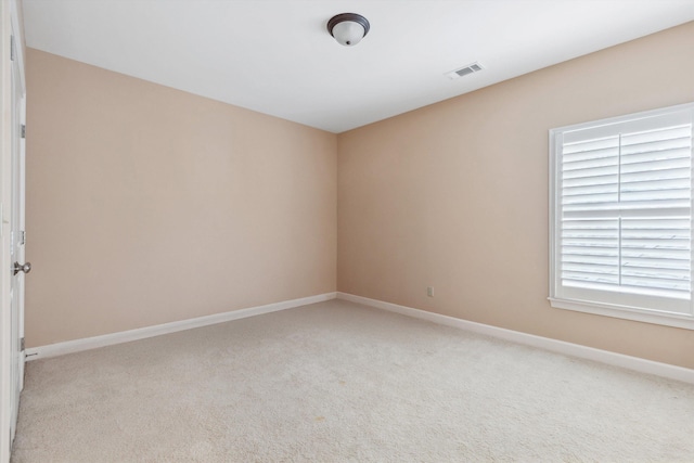 spare room featuring light colored carpet, visible vents, and baseboards