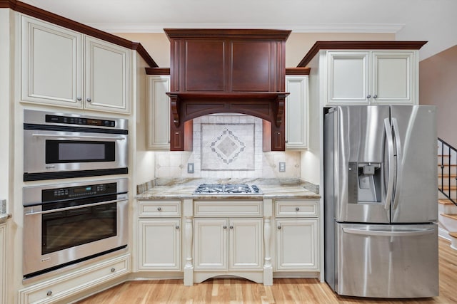 kitchen with ornamental molding, appliances with stainless steel finishes, light wood-type flooring, and tasteful backsplash