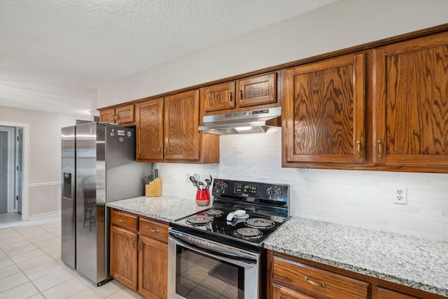 kitchen featuring brown cabinets, backsplash, appliances with stainless steel finishes, light stone countertops, and under cabinet range hood