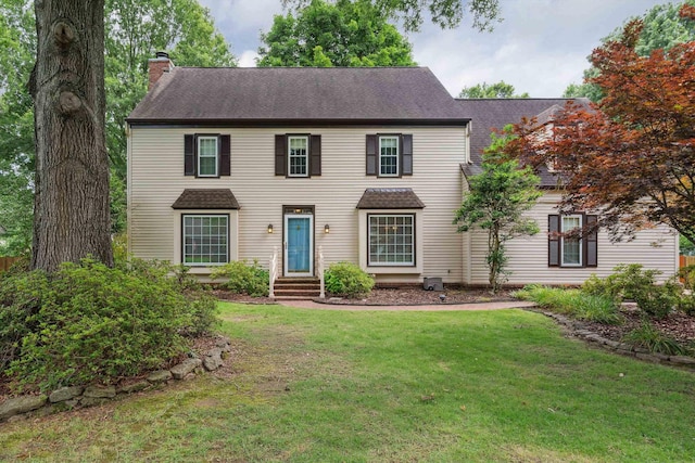 colonial-style house with a shingled roof, a chimney, and a front yard