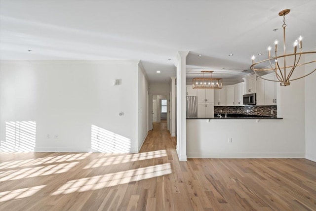 kitchen with stainless steel appliances, white cabinets, light wood-type flooring, tasteful backsplash, and dark countertops