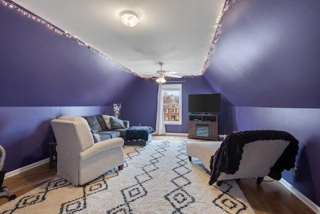 interior space featuring a ceiling fan, vaulted ceiling, baseboards, and wood finished floors