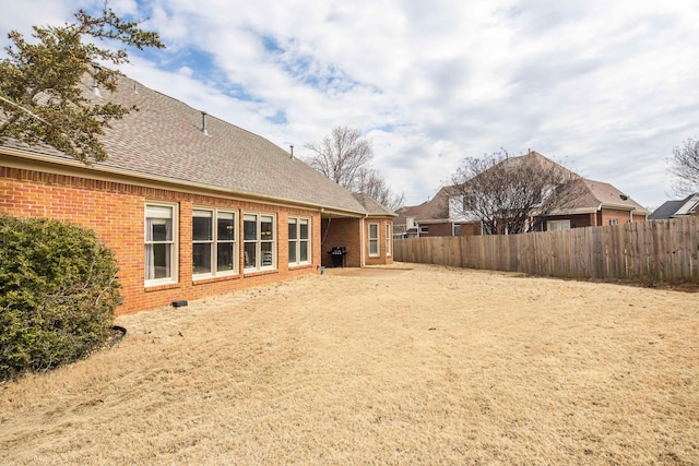 rear view of house with brick siding, fence, and roof with shingles