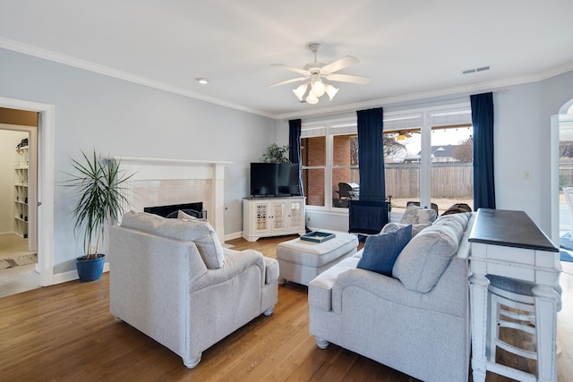 living area with a fireplace, wood finished floors, visible vents, baseboards, and ornamental molding