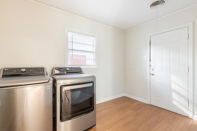 clothes washing area featuring laundry area, visible vents, baseboards, light wood finished floors, and washing machine and clothes dryer