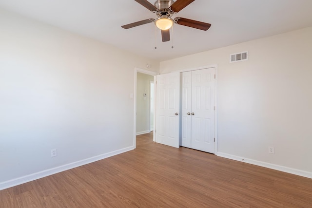 unfurnished bedroom with ceiling fan, wood finished floors, visible vents, baseboards, and a closet