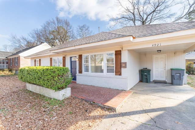 exterior space featuring a carport, a shingled roof, concrete driveway, and brick siding