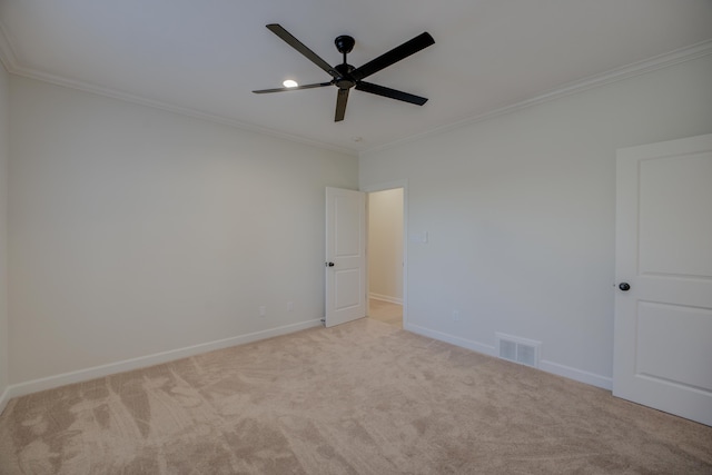 spare room with ceiling fan, light colored carpet, visible vents, baseboards, and ornamental molding