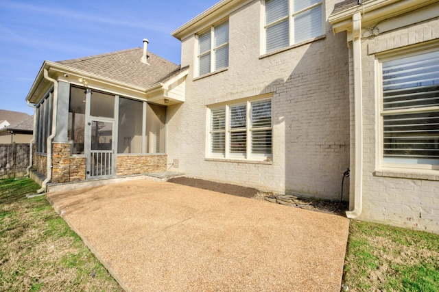 rear view of property featuring brick siding, roof with shingles, a patio area, and a sunroom