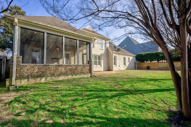 exterior space featuring fence, a sunroom, stone siding, a lawn, and stucco siding