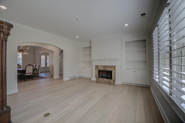 unfurnished living room with arched walkways, built in features, a premium fireplace, crown molding, and light wood-style floors