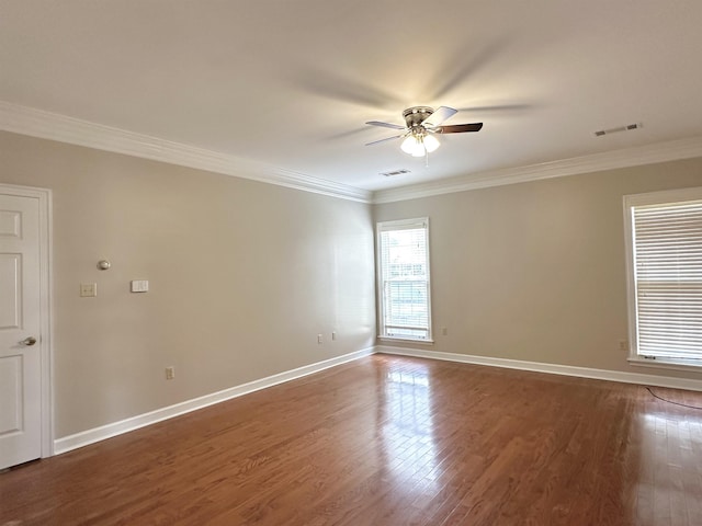 empty room with wood finished floors, visible vents, and crown molding