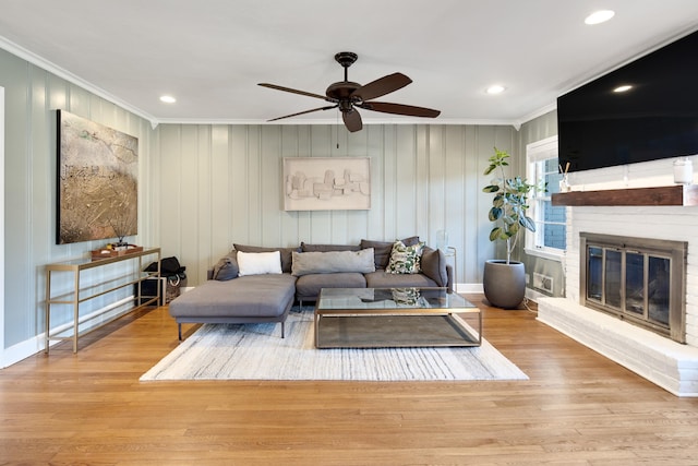 living area featuring a brick fireplace, ceiling fan, ornamental molding, and wood finished floors