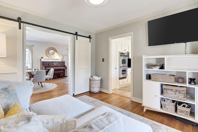 bedroom featuring light wood-style floors, ornamental molding, baseboards, and a barn door