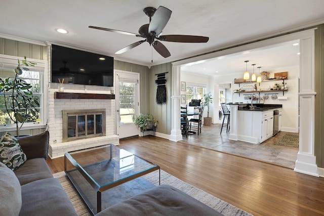 living room featuring a brick fireplace, baseboards, ornamental molding, and wood finished floors