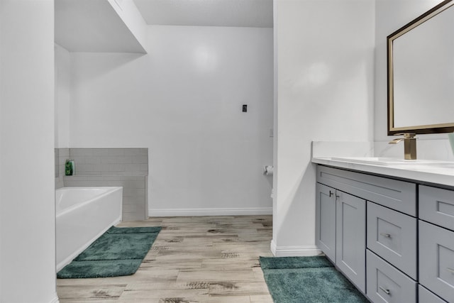 bathroom featuring wood finished floors, vanity, baseboards, and a bath