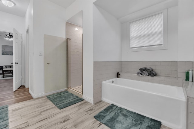 bathroom featuring baseboards, ceiling fan, wood finished floors, a tile shower, and a bath