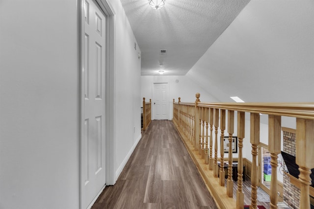 corridor featuring baseboards, visible vents, wood finished floors, vaulted ceiling, and a textured ceiling