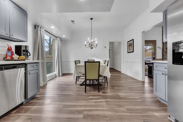 dining room with visible vents, wainscoting, light wood-style floors, a decorative wall, and a notable chandelier