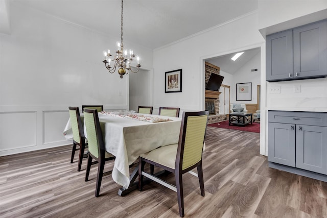 dining area featuring a notable chandelier, a decorative wall, a fireplace, wood finished floors, and ornamental molding