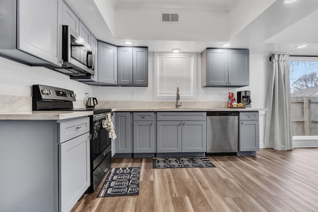 kitchen featuring gray cabinetry, stainless steel appliances, a sink, visible vents, and light wood-type flooring