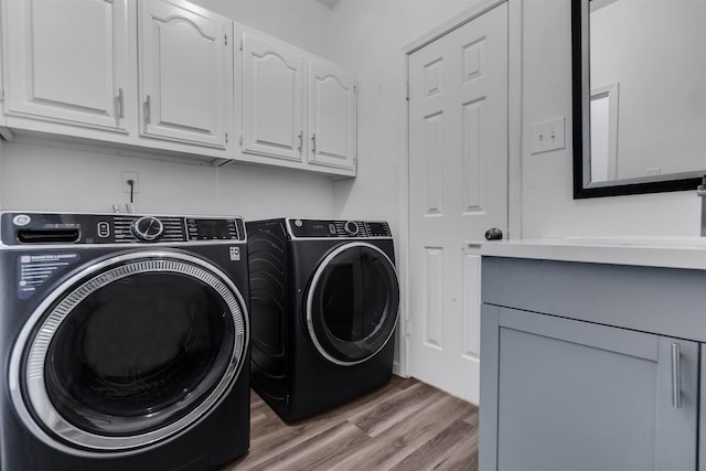 clothes washing area featuring wood finished floors, cabinet space, and washer and dryer