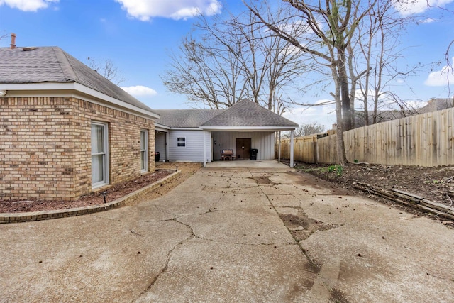 back of property featuring concrete driveway, brick siding, a shingled roof, and fence