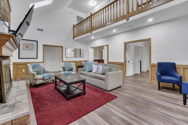 living room featuring wood finished floors, a towering ceiling, visible vents, wainscoting, and a brick fireplace