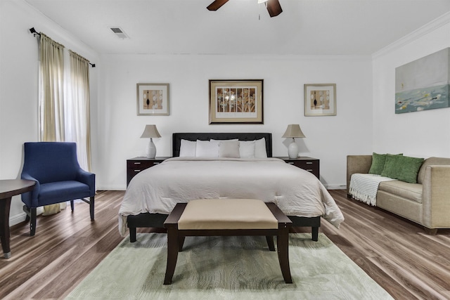 bedroom with ornamental molding, visible vents, baseboards, and wood finished floors