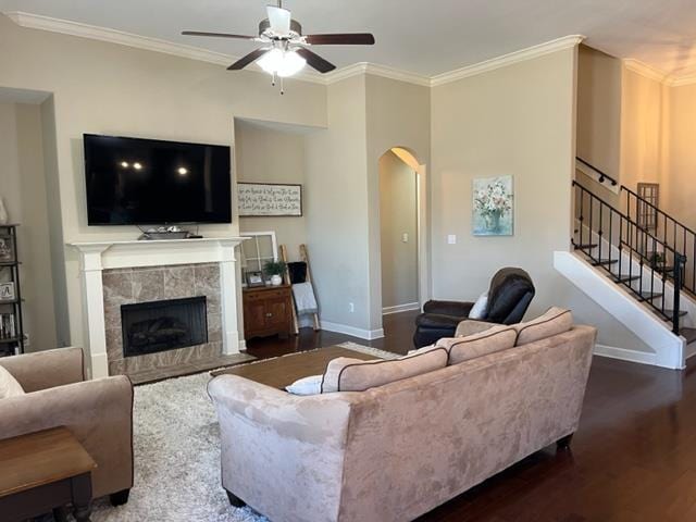 living room with baseboards, a tile fireplace, wood finished floors, stairs, and crown molding