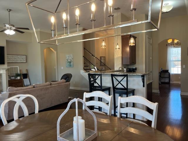 dining area featuring arched walkways, baseboards, dark wood-style floors, ceiling fan, and stairway