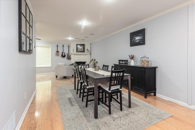 dining room with visible vents, baseboards, ornamental molding, a brick fireplace, and light wood finished floors