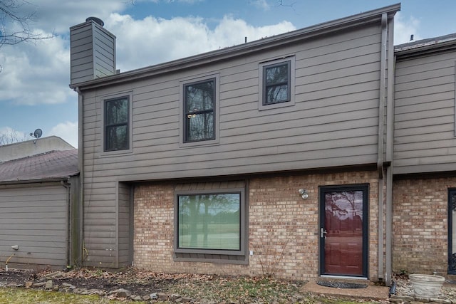 rear view of house featuring a chimney and brick siding