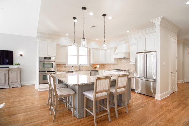 kitchen with a center island, stainless steel appliances, a sink, wall chimney range hood, and light wood-type flooring