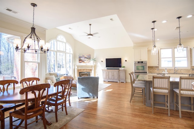 dining room featuring a fireplace, lofted ceiling, visible vents, ceiling fan, and light wood-type flooring