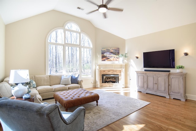 living room featuring a tiled fireplace, light wood finished floors, plenty of natural light, and visible vents