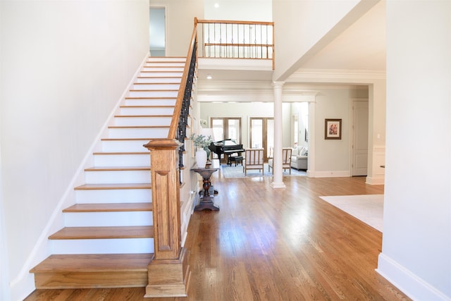 entrance foyer with baseboards, a towering ceiling, stairway, wood finished floors, and ornate columns