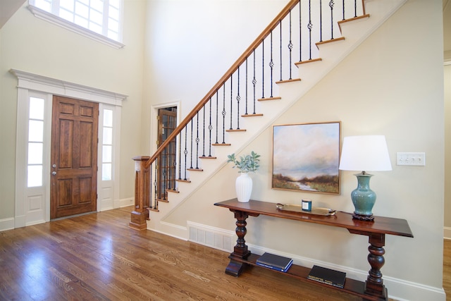 entrance foyer featuring visible vents, a high ceiling, wood finished floors, baseboards, and stairs