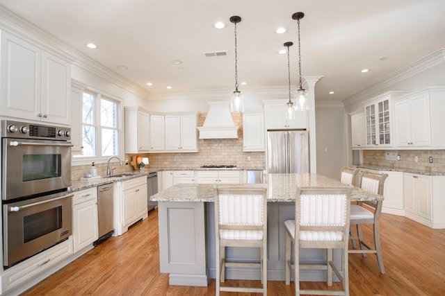 kitchen with appliances with stainless steel finishes, custom range hood, a sink, and light wood-style flooring