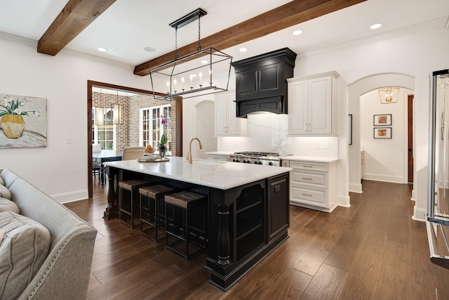 kitchen featuring arched walkways, light countertops, dark wood-type flooring, a sink, and beamed ceiling