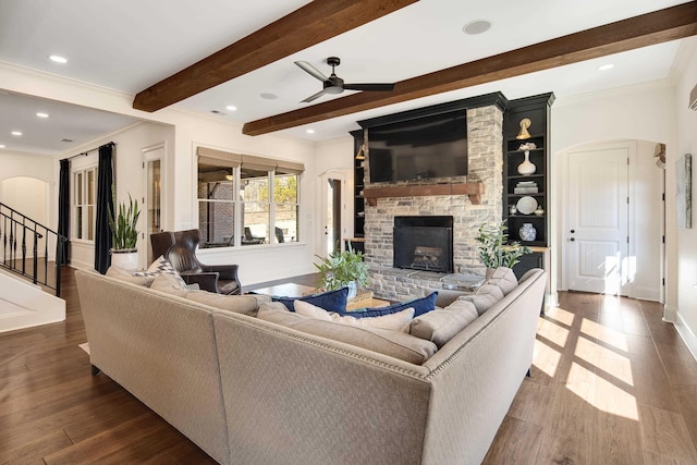 living room with arched walkways, beam ceiling, crown molding, dark wood finished floors, and a fireplace with raised hearth