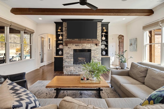 living area featuring dark wood-type flooring, arched walkways, a large fireplace, and beam ceiling