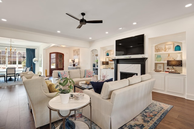 living room featuring arched walkways, hardwood / wood-style floors, crown molding, built in shelves, and recessed lighting